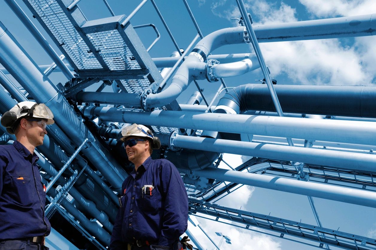 Two workers inspecting large industrial pipelines